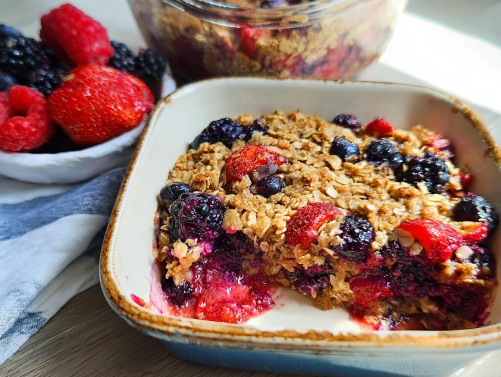 A serving of High Protein Triple Berry Bake in a dish, topped with oats and fresh berries.