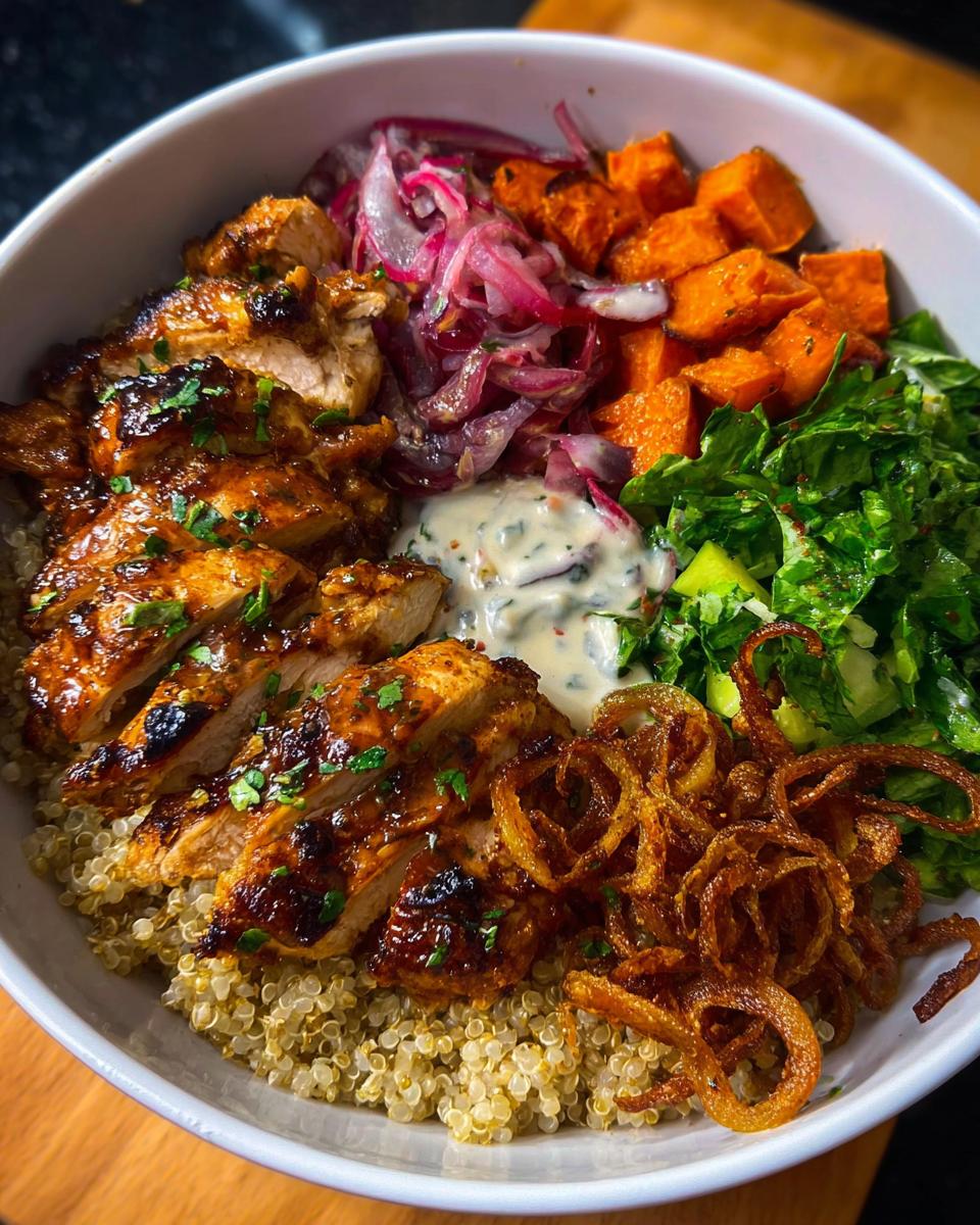 Close-up of a Hot Honey Chicken Bowl Recipe with sliced grilled chicken, quinoa, sweet potatoes, pickled onions, and greens.