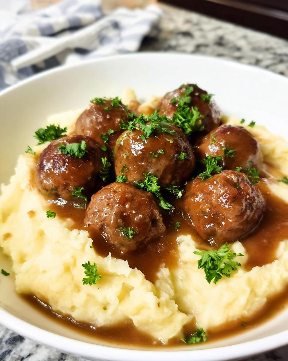 A bowl of Salisbury Steak Meatballs with Garlic Herb Mashed Potatoes, garnished with fresh parsley.