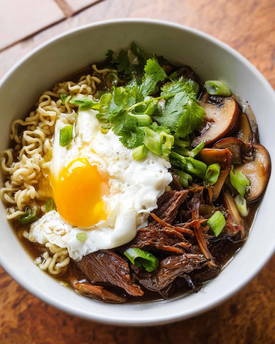A bowl of Slow Cooker Beef Ramen Noodles topped with a fried egg, sliced mushrooms, cilantro, and green onions.