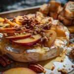 A wheel of baked brie topped with sliced peaches, toasted pecans, and drizzled with honey, served with toasted baguette slices.