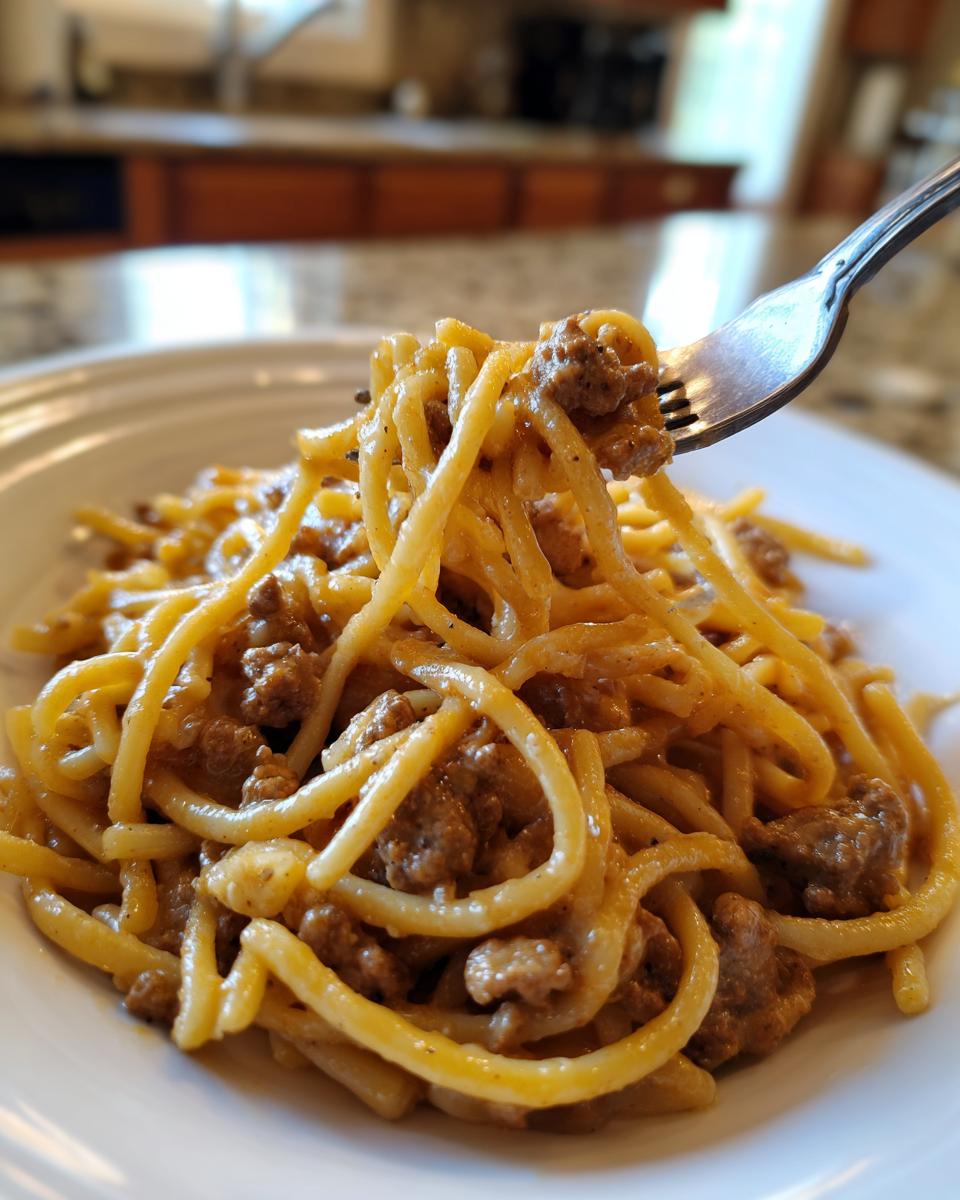 A fork lifting a portion of Creamy High Protein Beef Pasta from a white plate.
