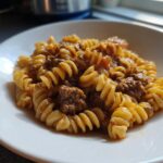 A close-up of a white bowl filled with creamy high protein beef pasta, featuring fusilli noodles and a rich meat sauce.