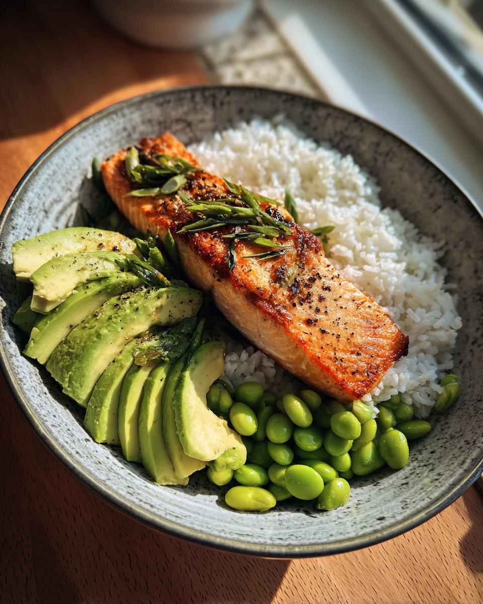 A close-up of a Crispy Salmon and Rice Bowl featuring a perfectly cooked salmon fillet, white rice, sliced avocado, and edamame.
