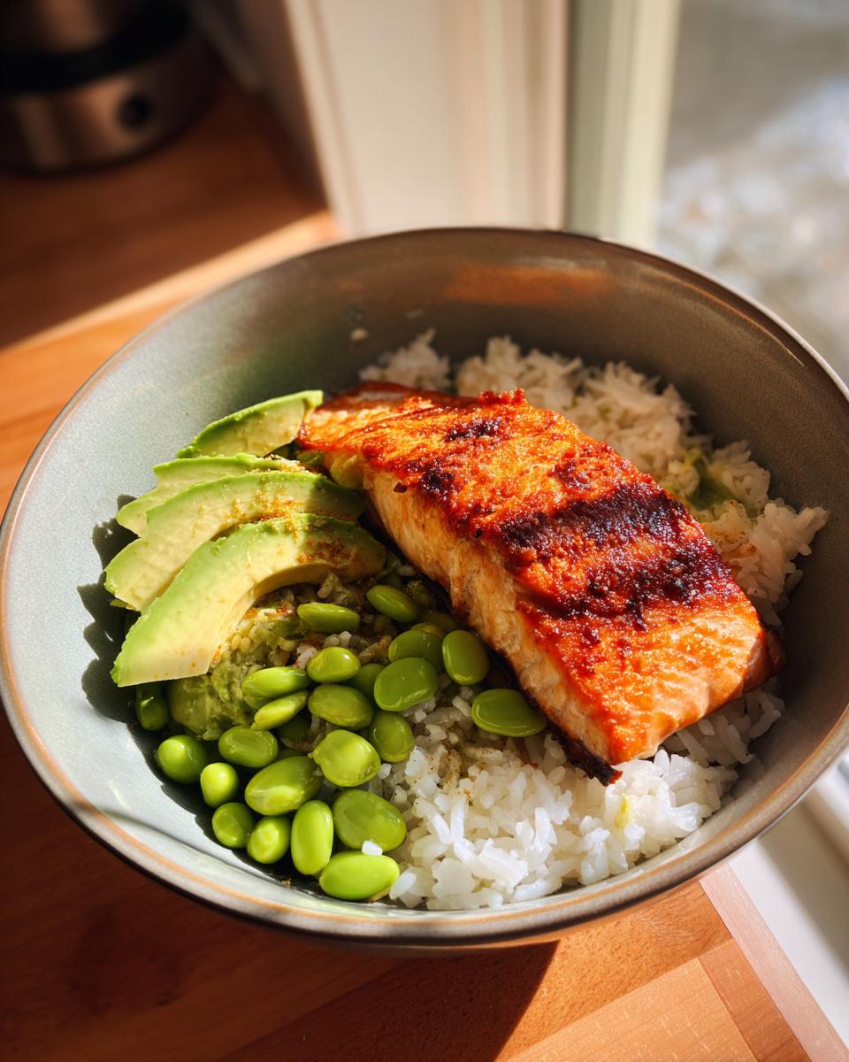 A close-up of a Crispy Salmon and Rice Bowl featuring a piece of perfectly cooked salmon, sliced avocado, edamame, and white rice.