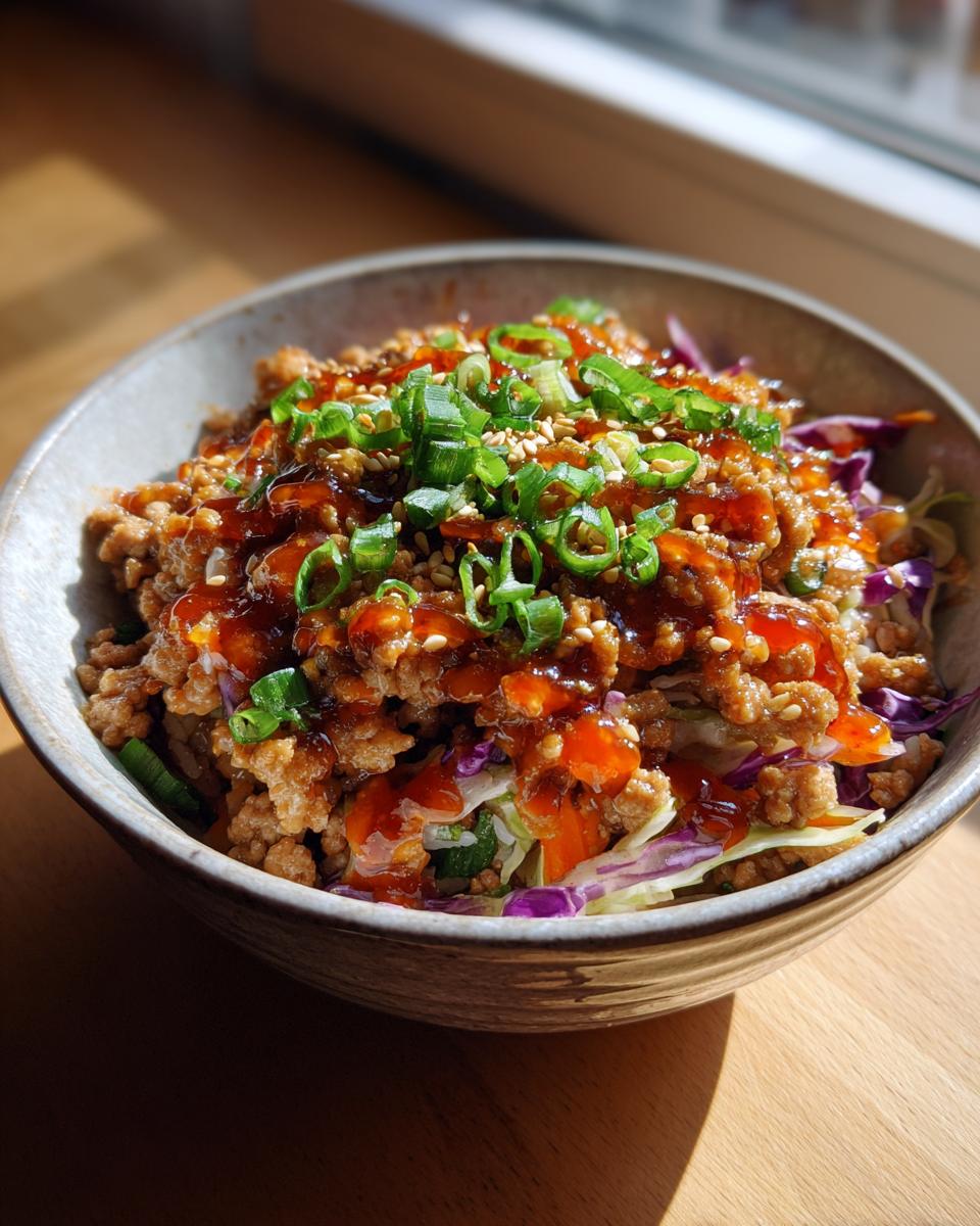 A close-up of a bowl filled with Egg Roll in a Bowl, topped with ground meat, vegetables, sauce, and green onions.