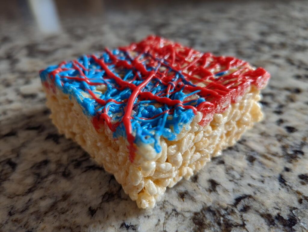 A single Firecracker Rice Krispie Treat decorated with red and blue icing, perfect for Fourth of July Desserts.