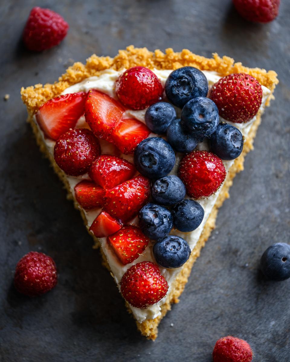 A slice of Fourth of July Flag Fruit Pizza on a cookie crust, topped with cream cheese frosting and fresh berries.