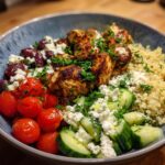 A vibrant bowl of Greek Chicken Bowls, featuring seasoned chicken, quinoa, cherry tomatoes, cucumbers, olives, and feta cheese.