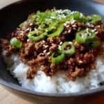 A close-up of a Korean Ground Beef Bowl, featuring seasoned ground beef over white rice, topped with sliced green onions and sesame seeds.