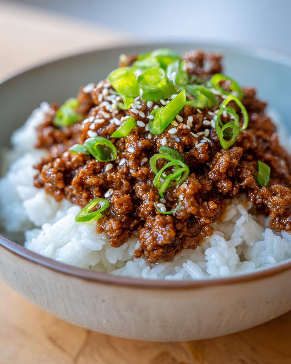 A close-up of a Korean Ground Beef Bowl, featuring seasoned ground beef over white rice, topped with sesame seeds and chopped green onions.