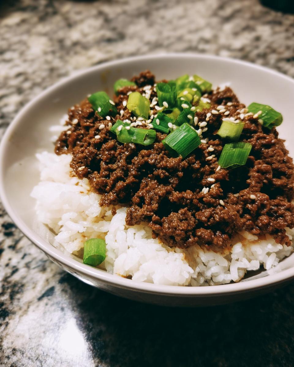 A close-up of a Korean Ground Beef Bowl, featuring seasoned ground beef over white rice, topped with chopped green onions and sesame seeds.