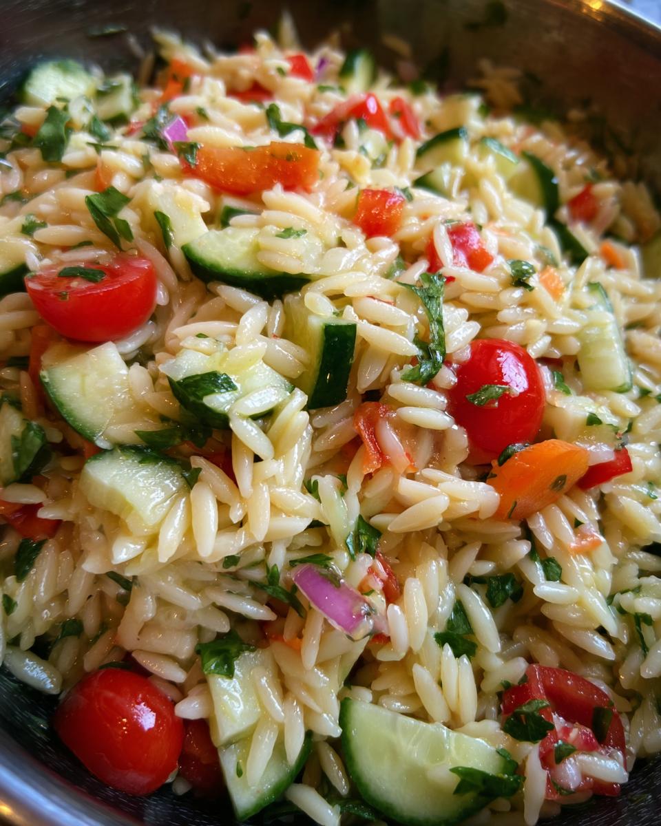 Close-up of a vibrant lemony orzo salad with fresh vegetables like cucumber, cherry tomatoes, and red onion.