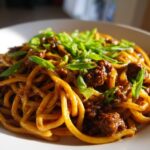 A close-up shot of a bowl of Mongolian Ground Beef Noodles, garnished with fresh green onions.