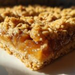 Close-up of a slice of peach crumble bars with a buttery oat topping and a gooey peach filling.