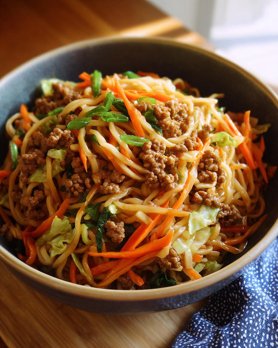 A close-up of a Potsticker Noodle Bowl with Pork & Cabbage Slaw, featuring noodles, ground pork, shredded carrots, and cabbage.