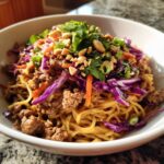 A vibrant bowl of Potsticker Noodle Bowl with Pork & Cabbage Slaw, featuring noodles, seasoned pork, red cabbage, carrots, and peanuts.