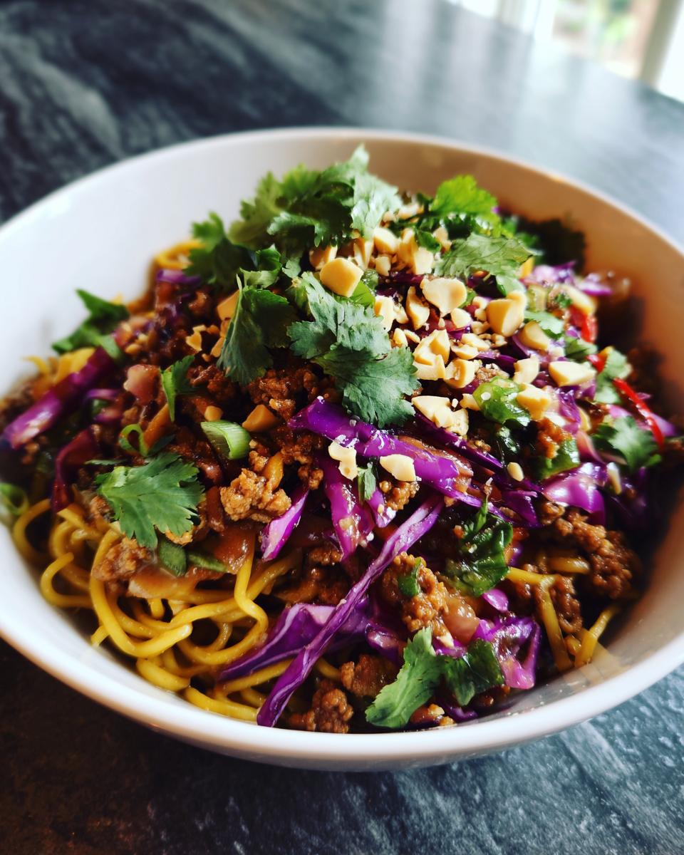 A close-up of a Potsticker Noodle Bowl with Pork & Cabbage Slaw, featuring noodles, ground pork, red cabbage, cilantro, and peanuts.
