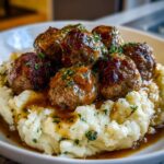 A plate of Salisbury Steak Meatballs served over creamy Garlic Herb Mashed Potatoes, drizzled with rich brown gravy and garnished with parsley.