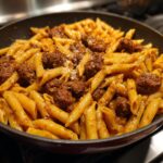 Close-up of a skillet filled with penne pasta and sausage in a sticky honey garlic sauce.