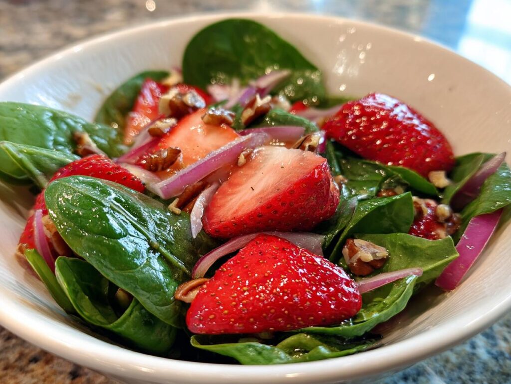 Close-up of a refreshing strawberry spinach salad with red onion and pecans in a white bowl.