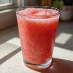 A tall glass filled with a vibrant pink, icy watermelon slushy drink, perfect for summer.